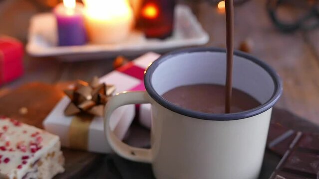 Hot chocolate pouring into a mug with cakes and gifts in the background