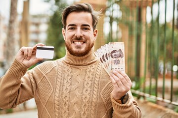 Young caucasian man holding mexican pesos banknotes and credit card at the city.