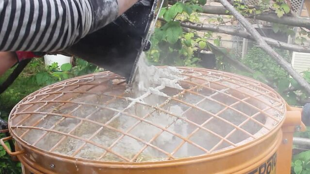 Man putting lime into a hempcrete mixer with a bucket and gloves