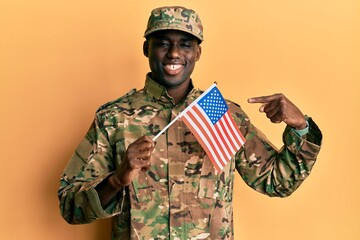 Fototapeta premium Young african american man wearing army uniform holding american flag smiling happy pointing with hand and finger