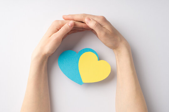 Stop the war in Ukraine concept. Top overhead view photo of girl's hands hugging yellow and blue hearts national flag colours on white background