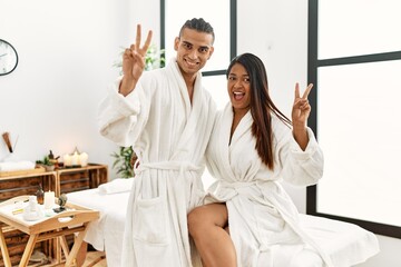 Young latin couple wearing towel standing at beauty center smiling with happy face winking at the...
