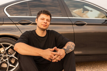 Fashion handsome man hipster sits and rest near a car. Travel by car