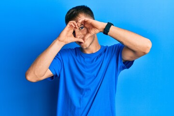 Young caucasian man wearing casual blue t shirt doing heart shape with hand and fingers smiling...