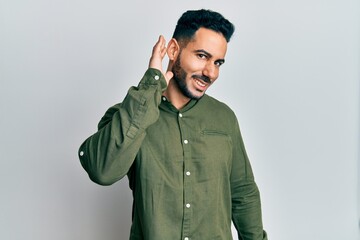 Fototapeta premium Young hispanic man wearing casual clothes smiling with hand over ear listening an hearing to rumor or gossip. deafness concept.