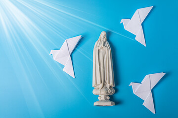 On a blue background is a statue of the Virgin Mary, three paper doves made in the origami technique. The concept of achieving peace through prayer