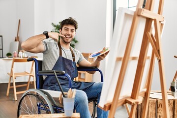 Fototapeta na wymiar Young hispanic man sitting on wheelchair painting at art studio smiling cheerful showing and pointing with fingers teeth and mouth. dental health concept.