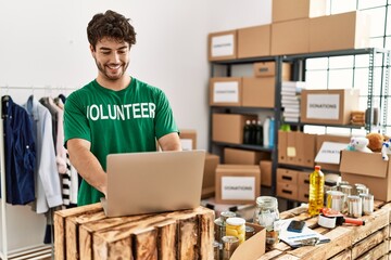 Young hispanic man wearing volunteer uniform using laptop at charity center