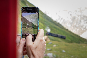 Tourist macht mit Smartphone ein Foto der sich nähernden Furka-Dampfbahn