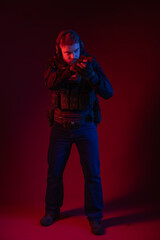 soldier in full gear with weapons. a man in headphones, body armor, with a backpack and a belt. red background. colored, blue-red light