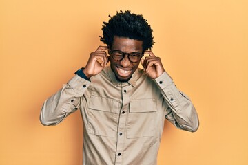 Young african american man wearing casual clothes and glasses covering ears with fingers with annoyed expression for the noise of loud music. deaf concept.