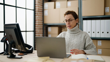Middle age hispanic woman ecommerce business worker using laptop at storehouse office