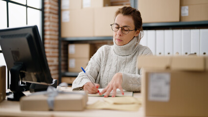Middle age hispanic woman ecommerce business worker writing on book at storehouse office