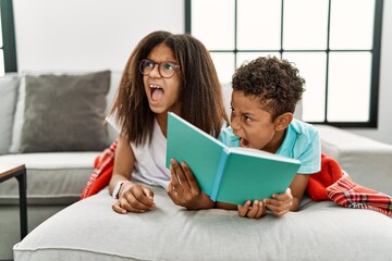 Two siblings lying on the sofa reading a book angry and mad screaming frustrated and furious,...