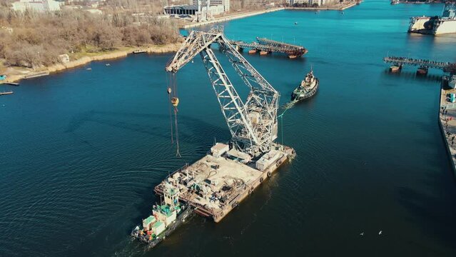 Aerial view tugboat pulling floating crane by river in city of shipbuilders. Logistics concept of water cargo transportation