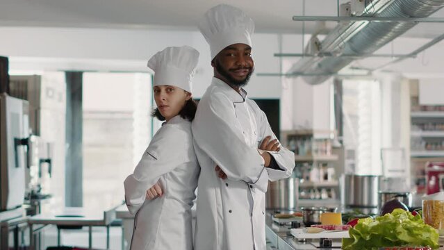 Portrait of man and woman chefs working on gourmet cuisine with meal preparations in restaurant kitchen. Multiethnic team of people cooking professional culinary food dish with ingredients.