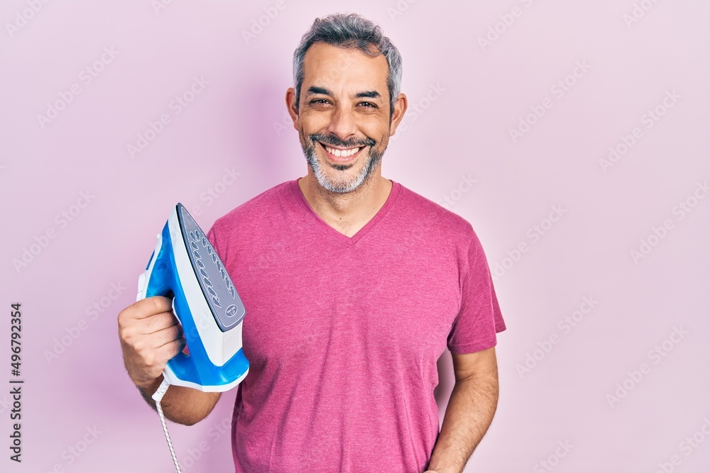 Sticker handsome middle age man with grey hair holding electric steam iron looking positive and happy standi