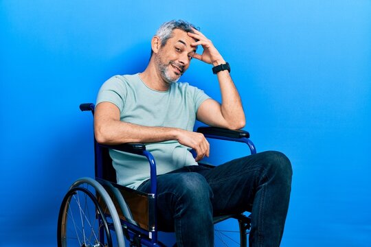 Handsome middle age man with grey hair sitting on wheelchair smiling confident touching hair with hand up gesture, posing attractive and fashionable