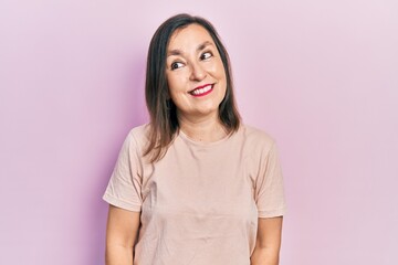 Fototapeta premium Middle age hispanic woman wearing casual clothes looking away to side with smile on face, natural expression. laughing confident.