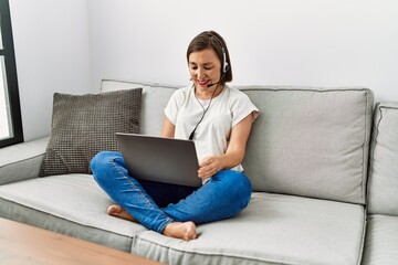 Naklejka premium Middle age hispanic woman sitting on the sofa wearing headset at home
