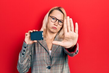 Beautiful caucasian blonde business woman holding ssd memory with open hand doing stop sign with serious and confident expression, defense gesture