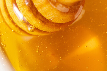 Wooden honey dipper with golden honey and air bubbles. Extreme close up, macro