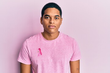 Young handsome hispanic man wearing pink cancer ribbon on shirt thinking attitude and sober expression looking self confident