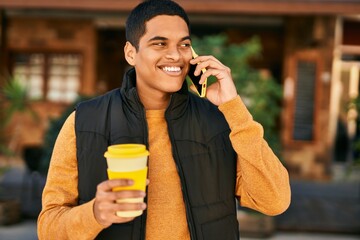 Young latin man talking on the smartphone and drinking coffee at the city