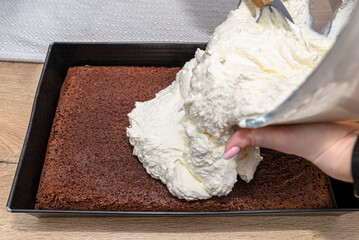 A woman pours the mixed curd and whipped cream into a baked cocoa cake in a baking tray.