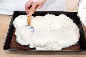 The woman uses a spoon to form the mixed curd and whipped cream on a baked cocoa cake on a baking...