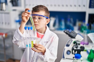 Blond child wearing scientist uniform holding test tubes at laboratory