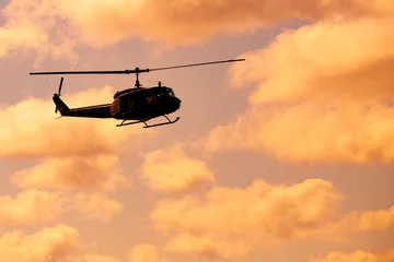 Selbstklebende Fototapeten Silhouette of the helicopter in the beautiful sky at sunset. © Nathan Jackson1/Wirestock Creators