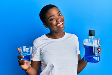 Young african american woman holding mouthwash for fresh breath winking looking at the camera with...