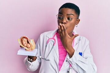 Young african american doctor woman holding anatomical model of female uterus with fetus covering...