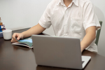 Remote work concept, Male freelancer reading business news on a book and working on laptop at home