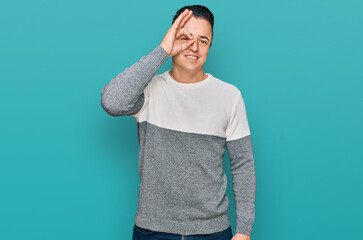 Handsome young man wearing casual winter sweater doing ok gesture with hand smiling, eye looking through fingers with happy face.