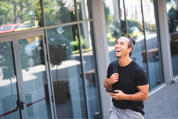 Man laughing and looking up while holding mobile phone and walking outdoors in city