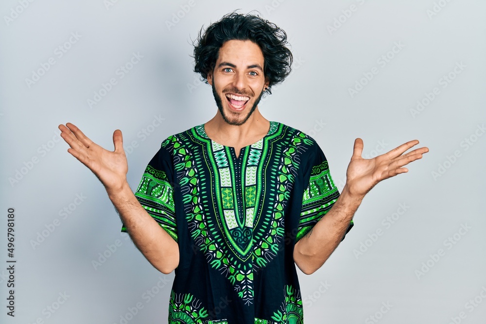 Sticker Handsome hispanic man wearing traditional african clothes celebrating victory with happy smile and winner expression with raised hands