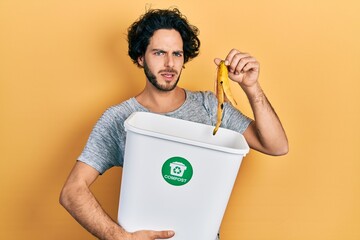 Handsome hispanic man recycling banana peel composting organic fertilizer clueless and confused...