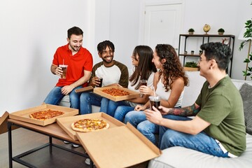 Group of young friends smiling happy eating italian pizza sitting on the sofa at home.