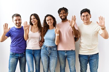 Group of young people standing together over isolated background waiving saying hello happy and smiling, friendly welcome gesture