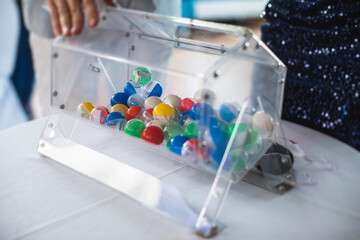 Process of prize drawings, extracting a winning numbers of lottery machine, raffle drum with bingo balls and winning tickets on event with a host and hands on lottery machine