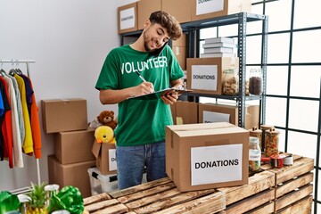 Young arab man wearing volunteer uniform talking on the smartphone writing on clipboard at charity center