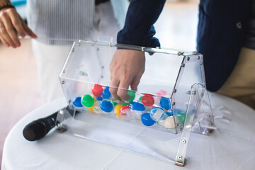 Process of prize drawings, extracting a winning numbers of lottery machine, raffle drum with bingo balls and winning tickets on event with a host and hands on lottery machine