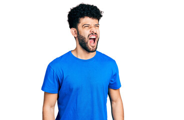 Young arab man with beard wearing casual blue t shirt angry and mad screaming frustrated and furious, shouting with anger. rage and aggressive concept.