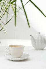 Tea in a white ceramic cup and a teapot on a white table.