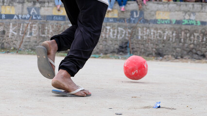 A boy playing football with a red soccer ball wearing flip-flops, close up of legs, footwear and...
