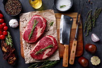 Raw ribeye beef steak with herbs on cutting board. Raw meat sirloin over dark stone background