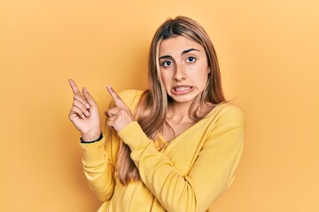 Beautiful hispanic woman wearing casual yellow sweater pointing aside worried and nervous with both...