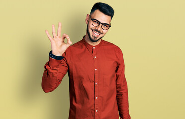 Young hispanic man with beard wearing business shirt and glasses smiling positive doing ok sign...